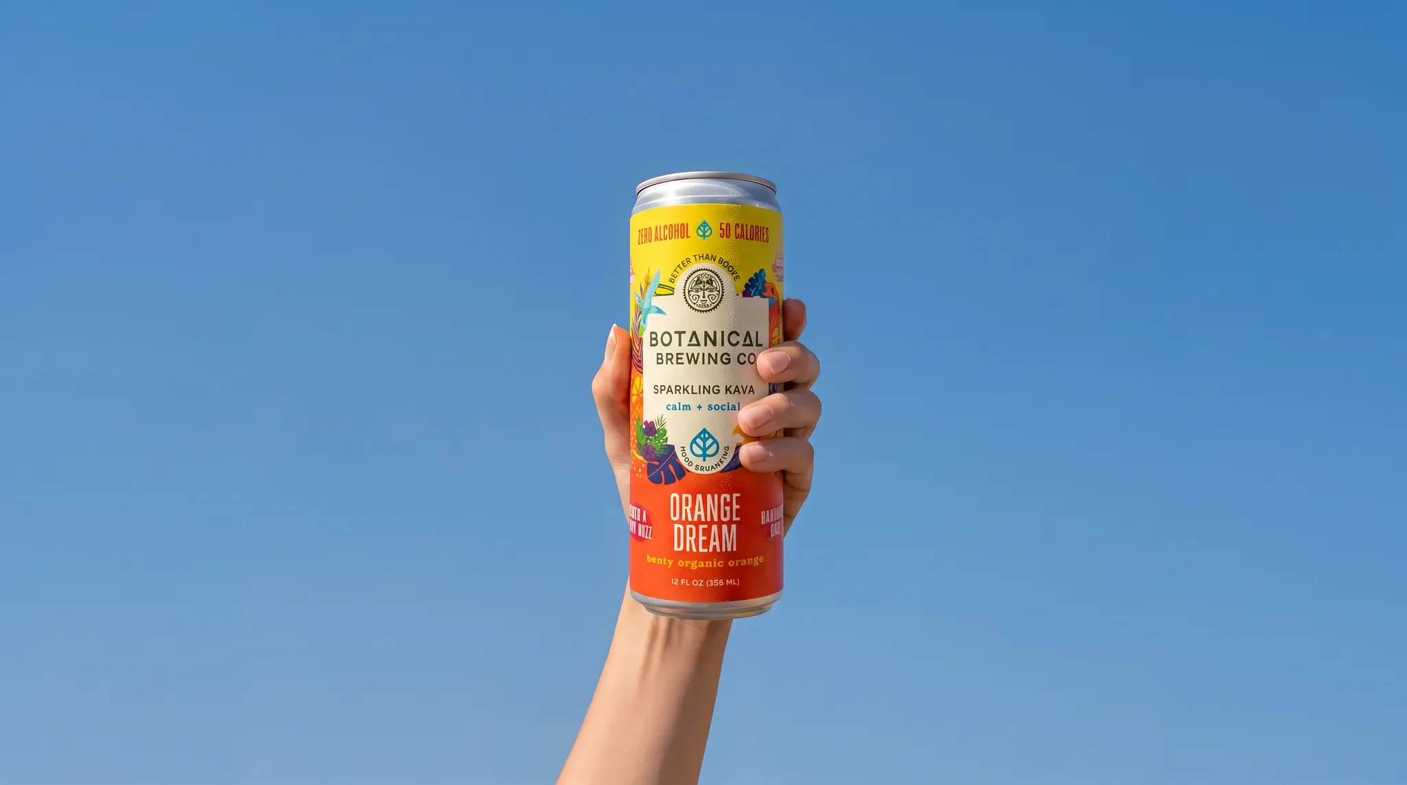 A hand holding a can of Botanical Brewing Co. Kava Orange Dream up against a clear blue sky