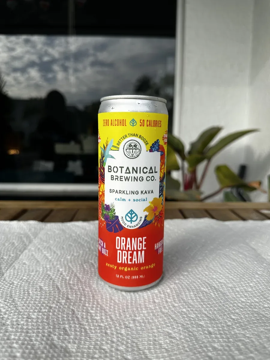 A can of Botanical Brewing Co. Kava Orange Dream on a table by a window